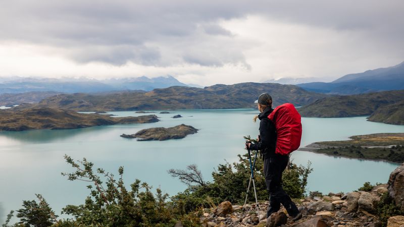 Hiker with trekking poles overlooking turquoise lakes and mountains at Valle Francés in Torres del Paine, Patagonia.