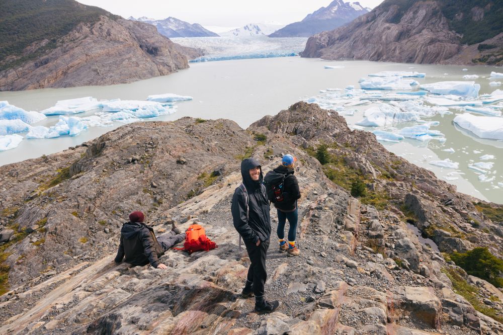 Hikers rest on a rocky summit overlooking Glaciar Grey's turquoise waters and icebergs in Torres del Paine, Patagonia.