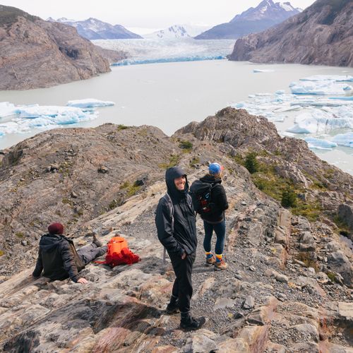 Hikers rest on a rocky summit overlooking Glaciar Grey's turquoise waters and icebergs in Torres del Paine, Patagonia.