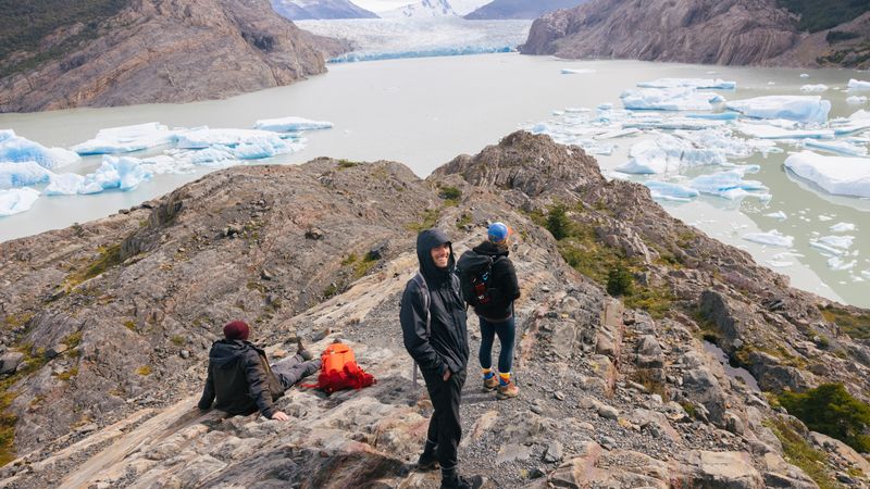 Hikers rest on a rocky summit overlooking Glaciar Grey's turquoise waters and icebergs in Torres del Paine, Patagonia.