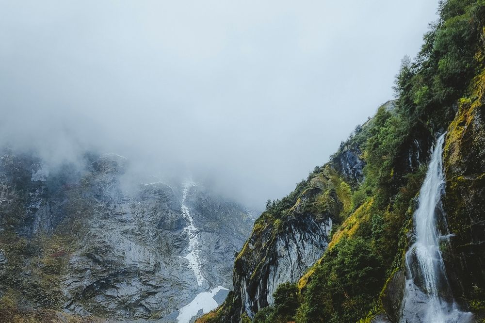 Misty mountain waterfall cascades into turquoise glacier-fed lake along Carretera Austral near Coyhaique, Patagonia.