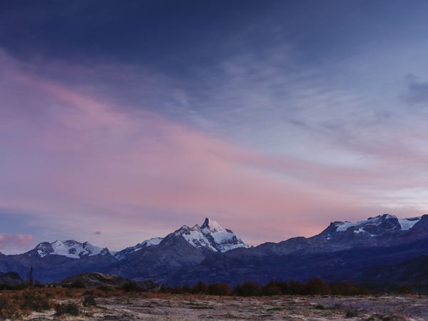Snow-capped peaks at dusk in Patagonia, with desert scrubland and colorful twilight sky over the Andes mountains.