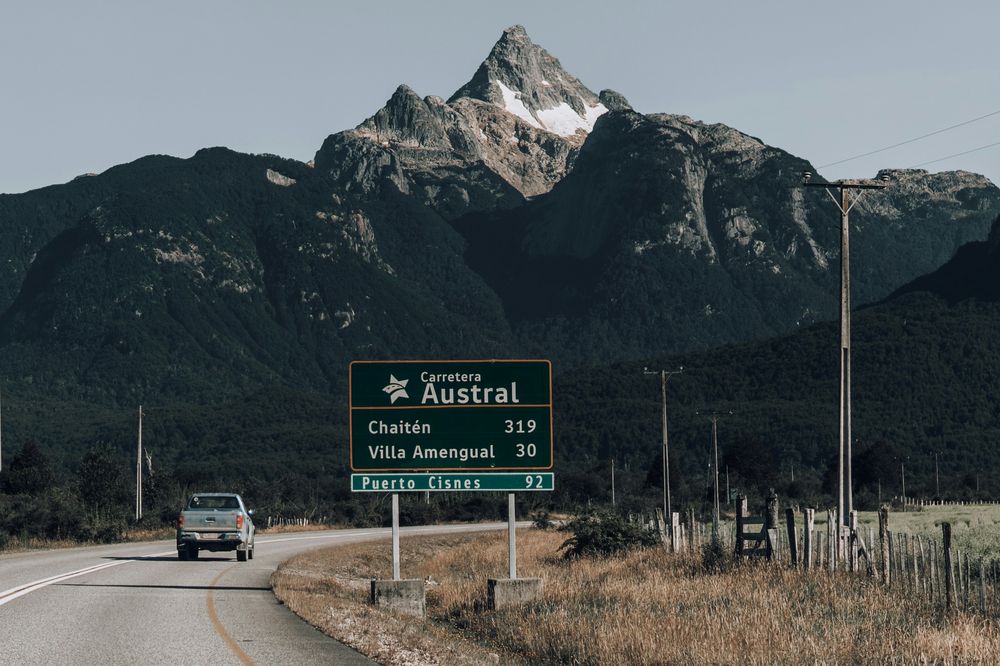 Carretera Austral road sign with snow-capped mountain peak and forested landscape in Patagonia, Chile.