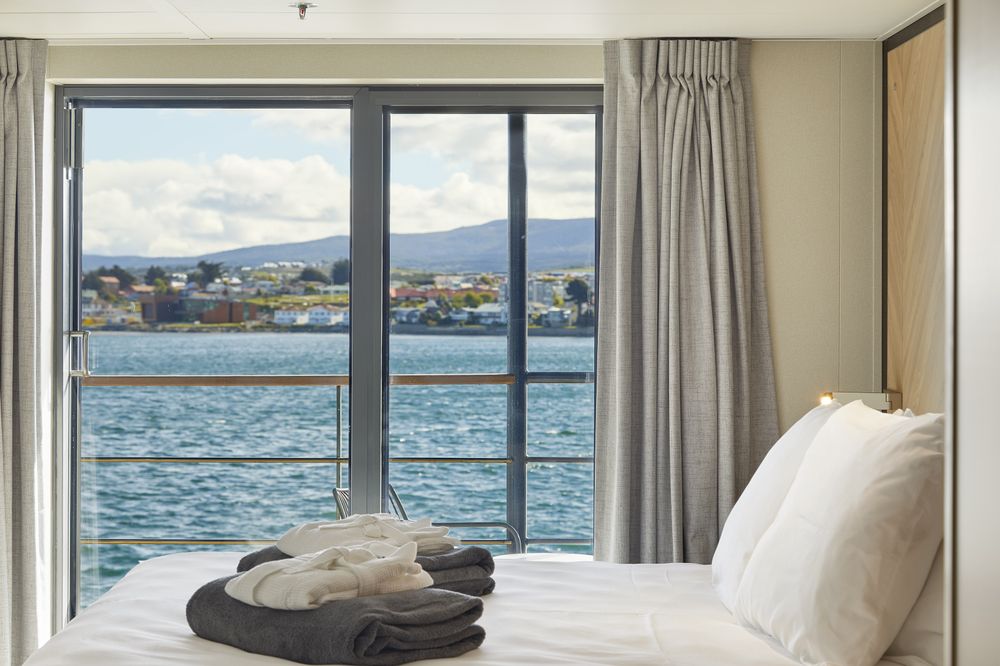 Luxury cabin bedroom overlooking the Beagle Channel with folded towels on the bed and mountain views in Ushuaia, Antarctica region.