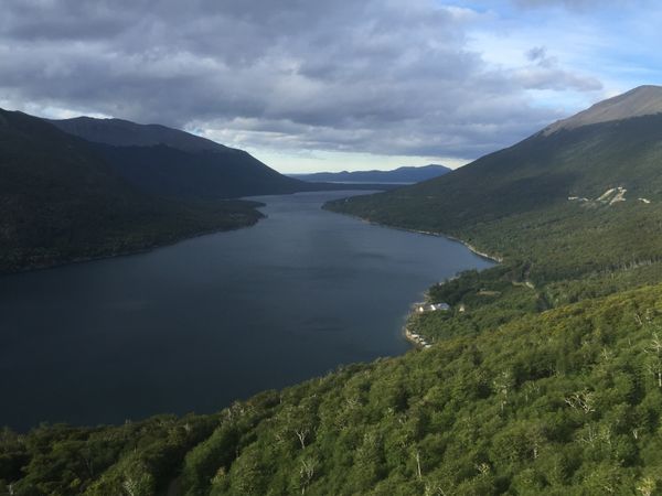 Deep forest valleys frame a pristine alpine lake nestled between snow-capped mountains in Patagonia's Lake District.