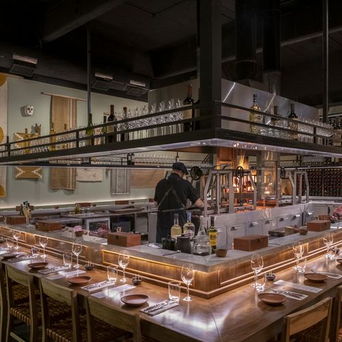Modern Argentine asado restaurant in Buenos Aires featuring an open kitchen with chef, long communal dining counter, and traditional wood-fired grill setup.
