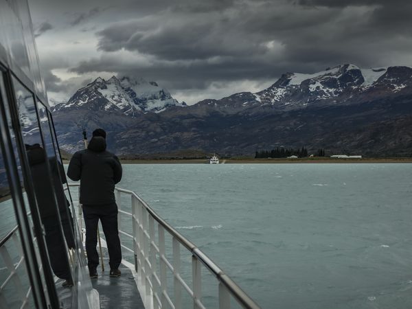 Traveler gazing at snow-capped Patagonian mountains from a boat on turquoise glacial waters near Estancia Cristina.