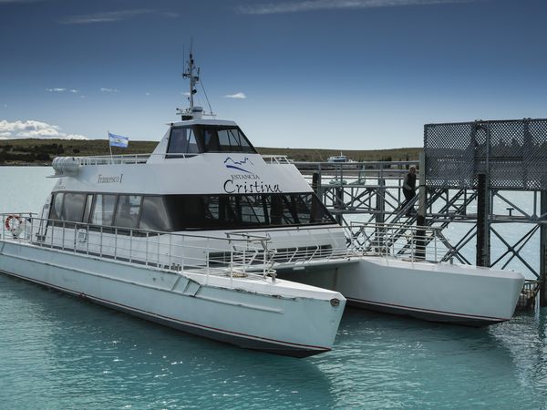 Estancia Cristina catamaran docked at turquoise waters in Patagonia, Argentina with snow-capped mountains visible.