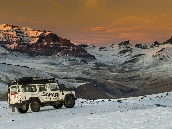 White safari vehicle parked in snowy Patagonian landscape with dramatic snow-capped mountains at golden hour.
