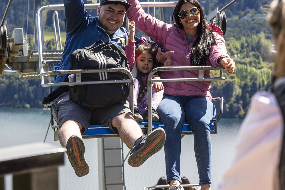 Family enjoying a scenic chairlift ride over forested mountains and lake near Bariloche, Argentina.