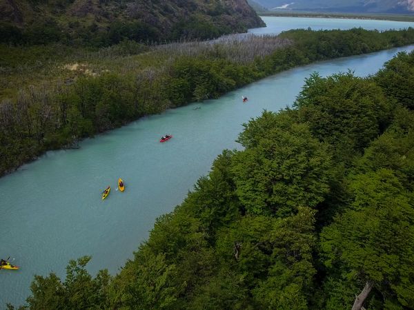 Kayakers paddle turquoise waters of Río de las Vueltas surrounded by dense forests and mountain peaks in Patagonia.