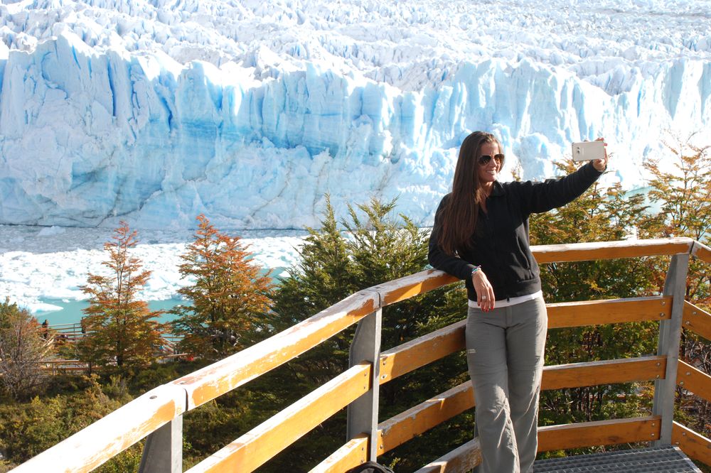 Woman taking a selfie on the viewing platform overlooking the stunning blue ice formations of Glaciar Perito Moreno in El Calafate, Patagonia.