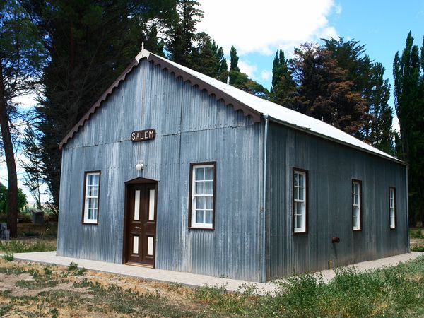 Historic Salem chapel with corrugated metal siding surrounded by cypress trees in Valle Inferior, Patagonia.