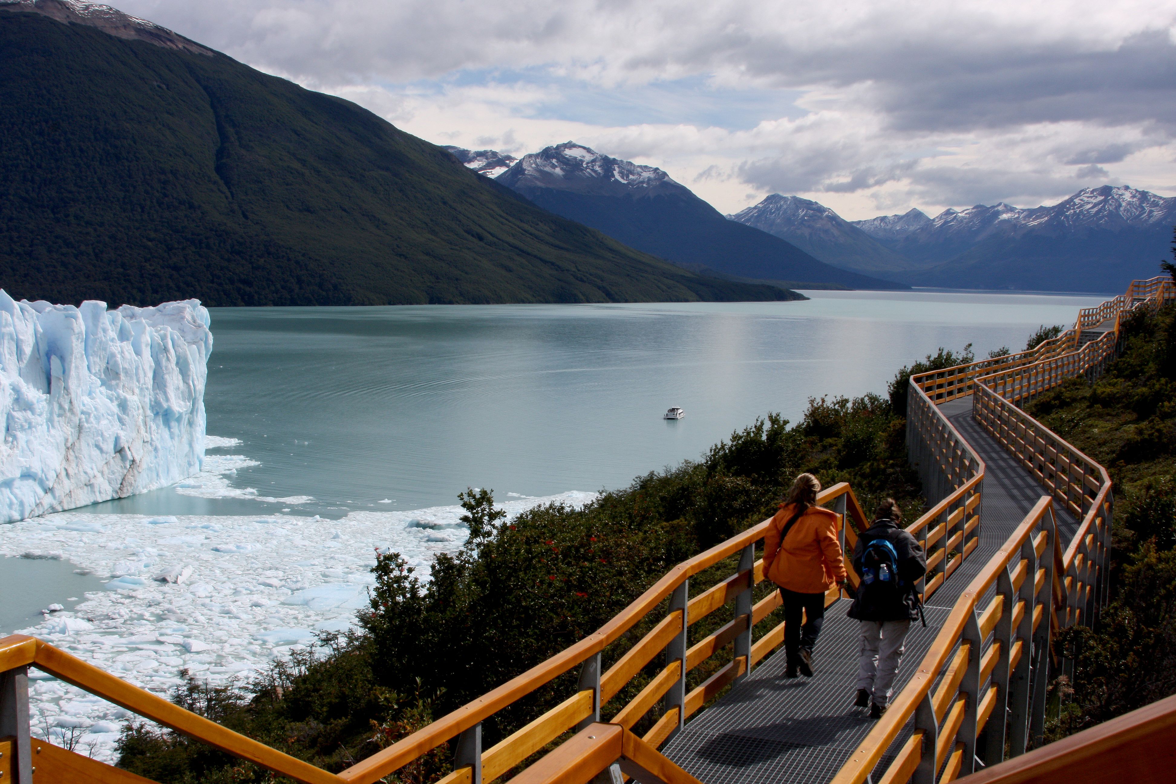 Wooden boardwalk overlooks turquoise waters and Glaciar Perito Moreno with snow-capped Andes mountains in El Calafate, Patagonia.
