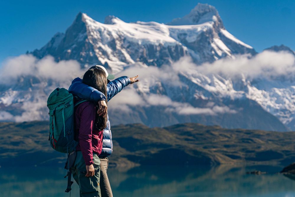 Hiker with backpack pointing toward snow-capped peaks of Torres del Paine in Patagonia, Chile.