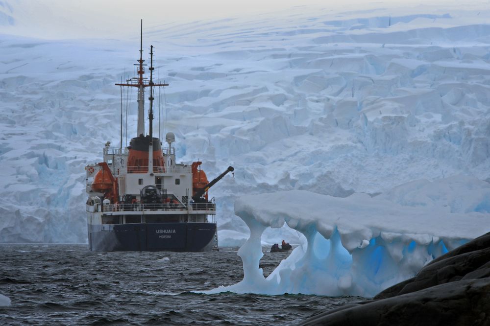 Research vessel Ushuaia navigates icebergs near Antarctic glacier formations in pristine polar waters.