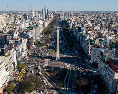 Aerial view of Buenos Aires showing the Obelisk monument, wide Avenida 9 de Julio, and sprawling cityscape under clear skies.