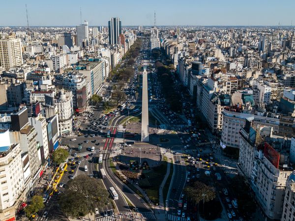 Aerial view of Buenos Aires showing the Obelisk monument, wide Avenida 9 de Julio, and sprawling cityscape under clear skies.