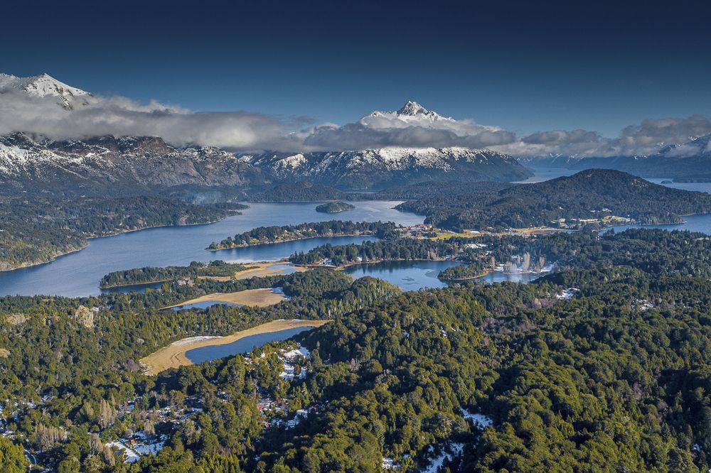 Aerial view of Bariloche's Circuito Chico with snow-capped Andes peaks, pristine lakes, and dense forests in Patagonia.