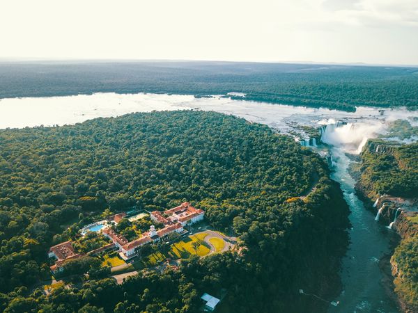 Aerial view of Belmond hotel nestled in lush rainforest overlooking Iguazú Falls and the Paraná River.