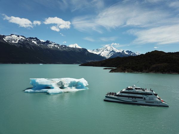 Tourist boat near icebergs on turquoise Lago Argentino with snow-capped Andes mountains in Patagonia.