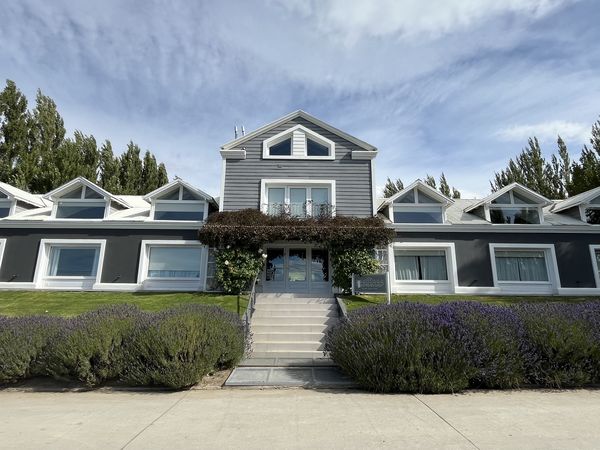 Modern hotel building Los Ponchos with lavender gardens and tall poplar trees under Patagonian sky.