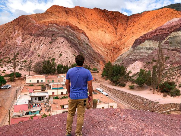 Traveler overlooking colorful striped mountains and village buildings in Paleta del Pintor, Purmamarca, Argentina.
