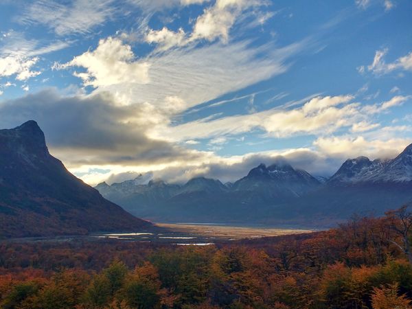Autumn forest and mountain lakes landscape in Patagonia with snow-capped peaks under dramatic cloudy sky.