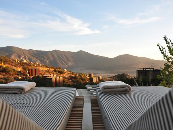 Luxury outdoor beds overlook arid mountains and a lake valley at a high-altitude Patagonian resort at sunset.