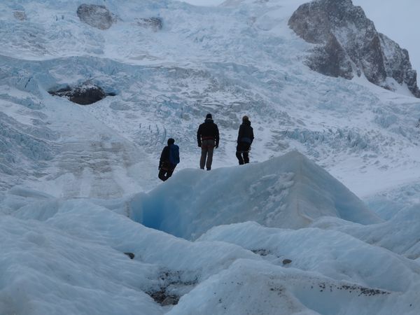 Three hikers traverse the blue ice formations and crevasses of Glaciar Cagliero in Patagonia.