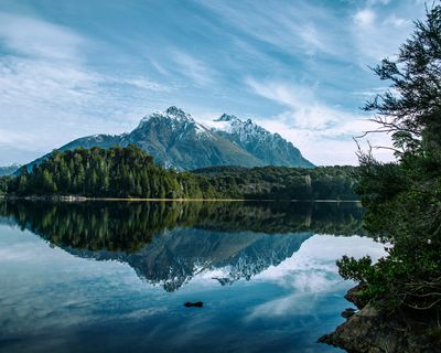 Snow-capped mountain reflected in calm lake waters surrounded by dense forest near Bariloche, Patagonia.