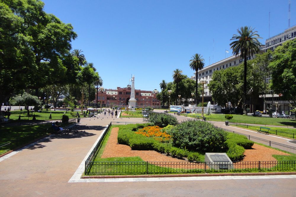 Plaza de Mayo in Buenos Aires featuring the iconic pink Casa Rosada government building surrounded by palm trees and manicured gardens.