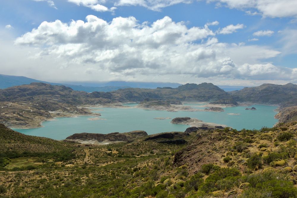 Turquoise glacial lake surrounded by rocky mountains and sparse vegetation along Carretera Austral in Patagonia.
