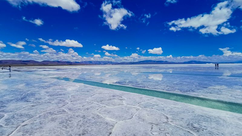 Turquoise water channels wind through the white salt flats of Salinas Grandes under a brilliant blue sky.