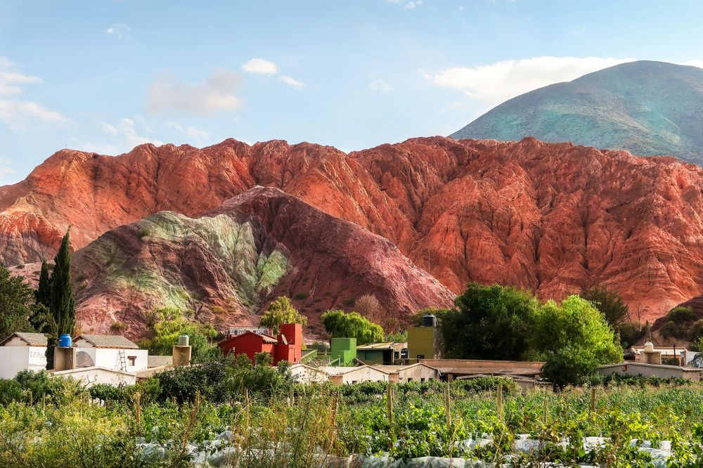 Colorful rock formations tower behind a small village with traditional buildings and gardens in Purmamarca, Argentina.