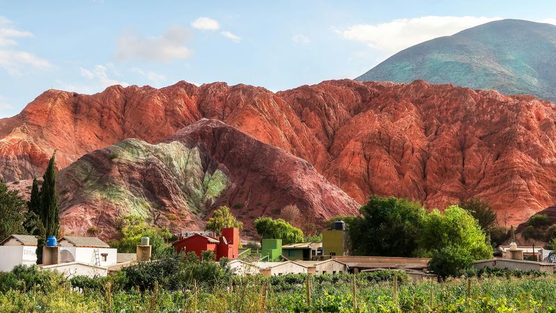 Colorful rock formations tower behind a small village with traditional buildings and gardens in Purmamarca, Argentina.