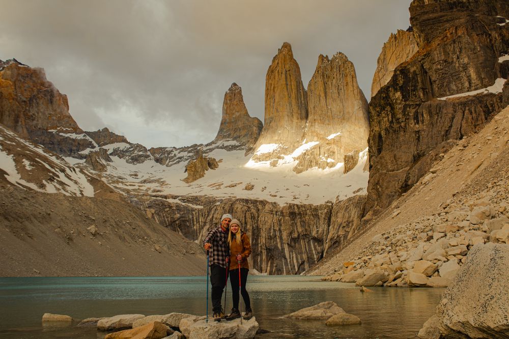 Hikers pose at Laguna Torre with the iconic granite towers of Torres del Paine rising dramatically behind them in Patagonia.