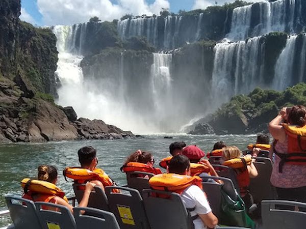 Tourists in life jackets on a boat tour approach the massive cascading waterfalls of Iguazú Falls.