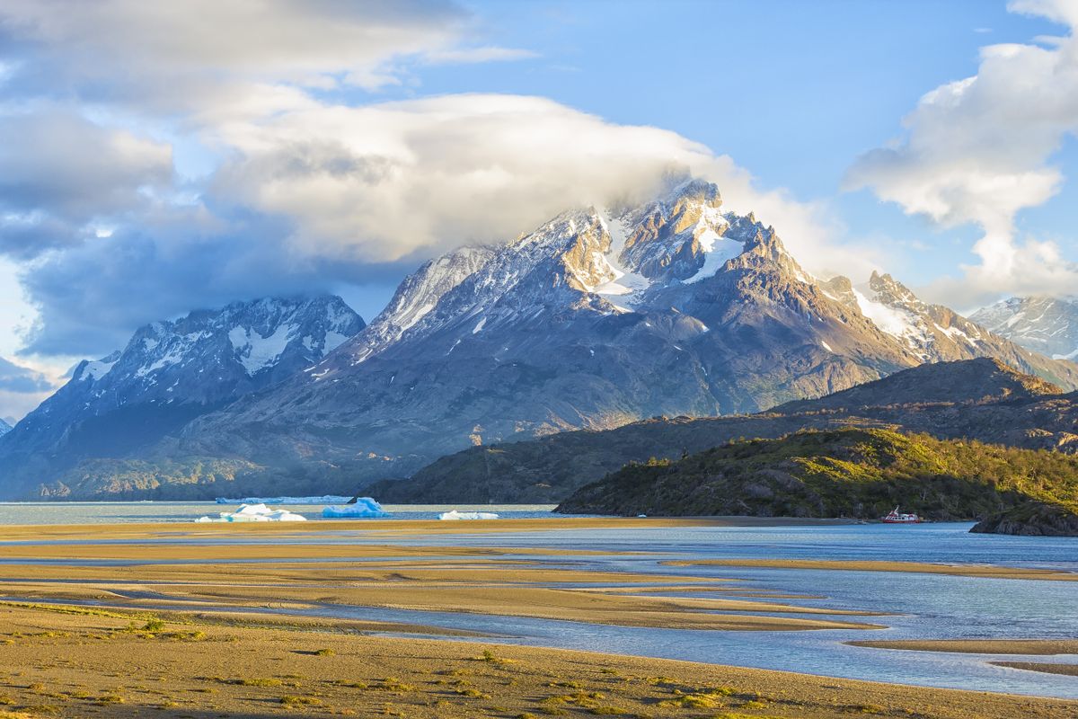 Snow-capped peaks of Torres del Paine rise above Glaciar Grey with icebergs floating in pristine waters under blue skies.