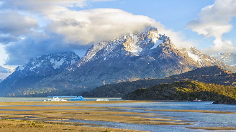 Snow-capped peaks of Torres del Paine rise above Glaciar Grey with icebergs floating in pristine waters under blue skies.