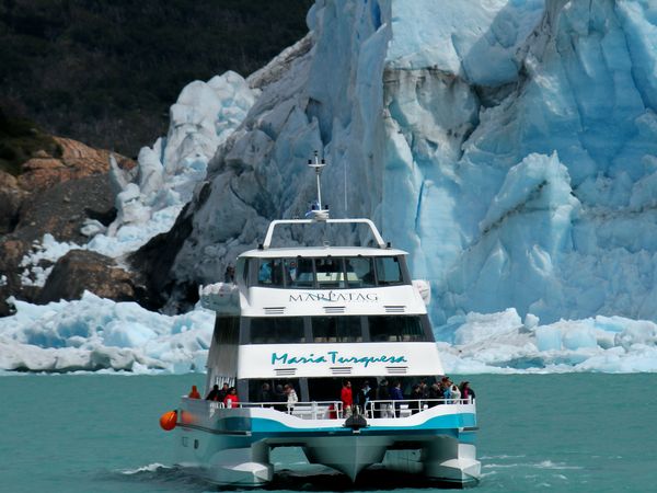 Catamaran cruise near a massive blue glacier in Patagonia with tourists on deck and turquoise glacial waters.