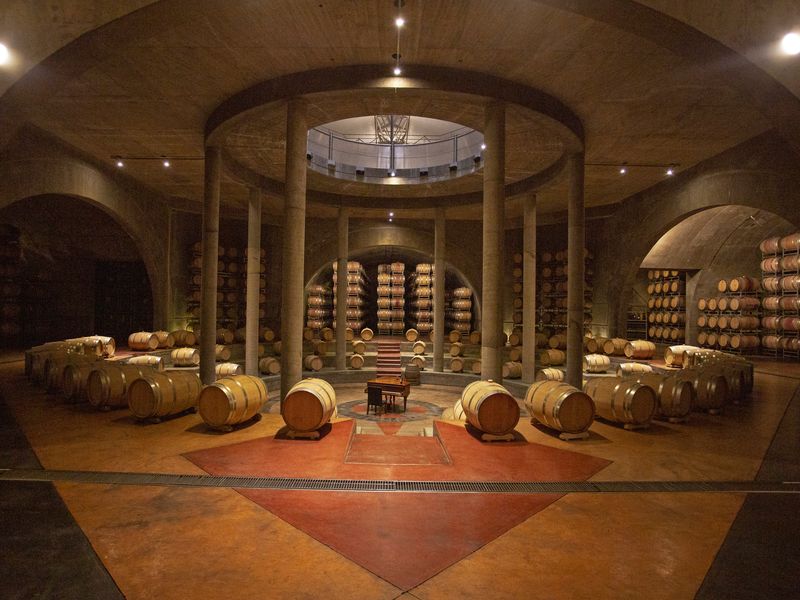 Underground wine cellar in Mendoza with wooden barrels, stone columns, and traditional winery architecture.
