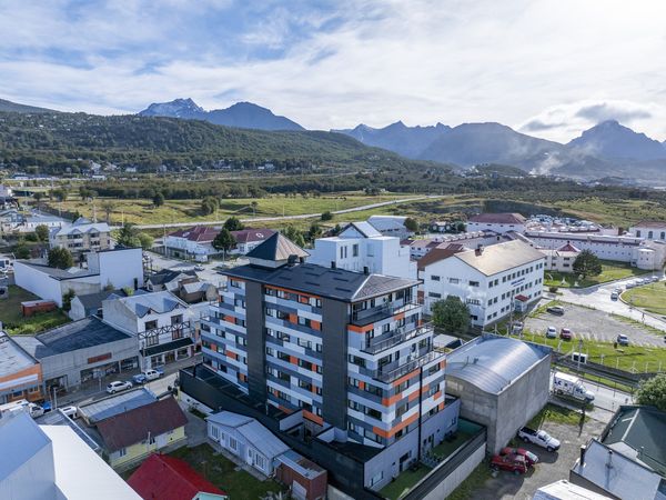 Modern apartment building in Ushuaia with snow-capped Andes mountains rising behind a scenic valley landscape.