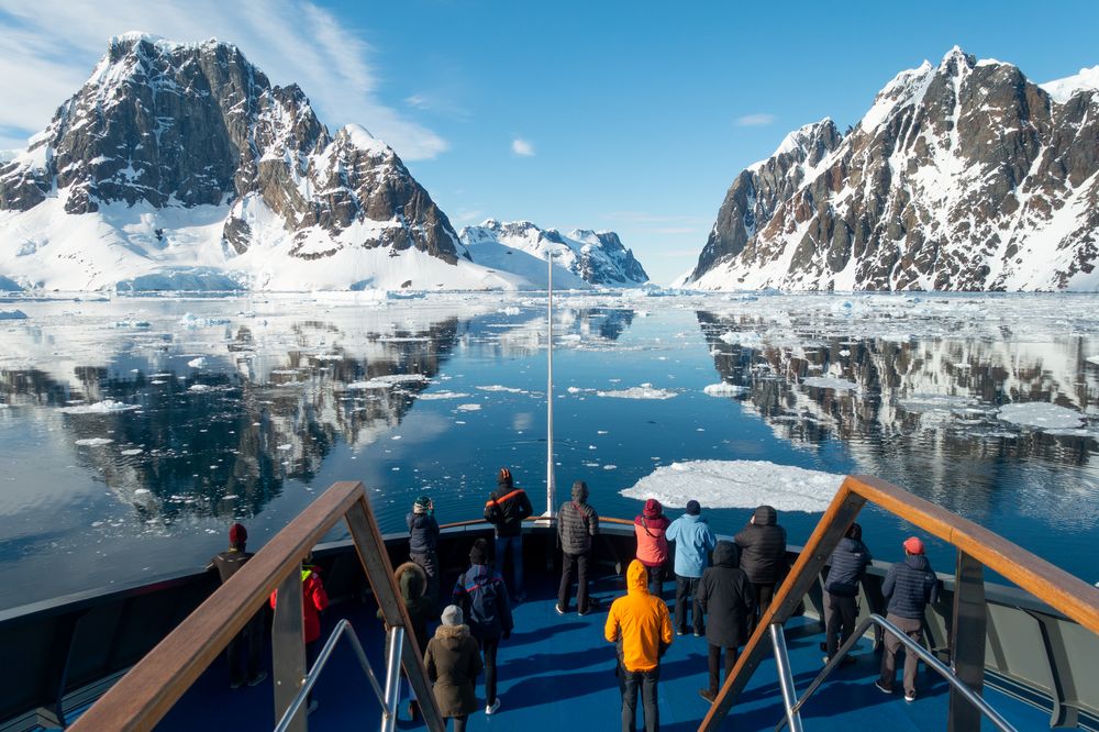 Tourists on a cruise ship deck viewing snow-capped mountains and icebergs in Antarctica's pristine polar waters.