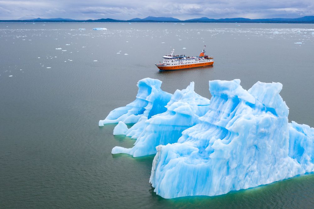 Orange expedition ship navigating near the brilliant blue ice formations of Glaciar San Rafael in Chilean Patagonia.