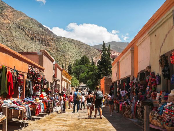 Colorful textile market in Purmamarca with orange colonial buildings and Andean mountains in the background.