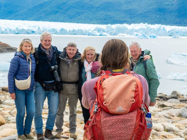 Tour guide with backpack photographs a group of travelers posing before Glaciar Perito Moreno's icy landscape in Patagonia.