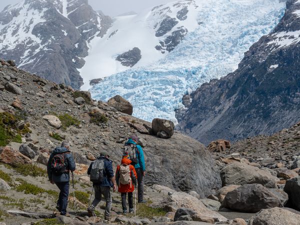 Three trekkers hiking toward Glaciar Sur with snow-capped peaks and blue ice formations in Patagonia.