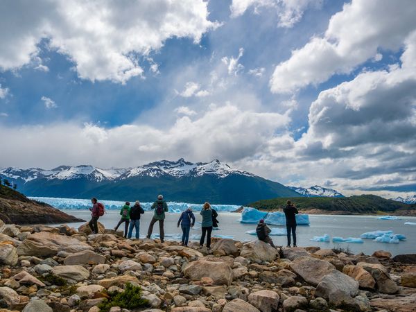 Tourists viewing icebergs and Glaciar Perito Moreno from rocky shoreline in Patagonia, Argentina.