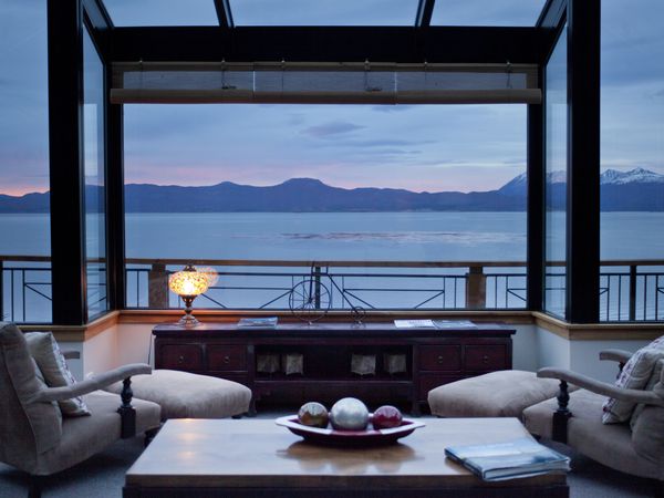 Luxury lakeside lounge at Los Cauquenes resort overlooking Nahuel Huapi Lake and Andes mountains at dusk.